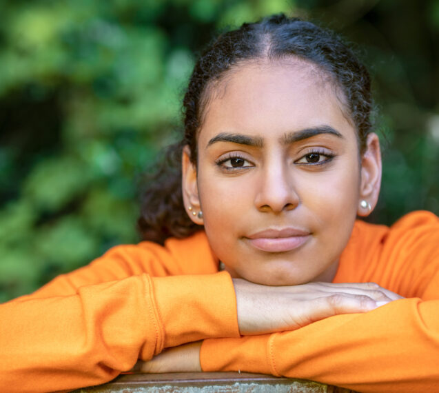 A young mixed race girl in a orange top looks at the camera to show she has overcome coercive control