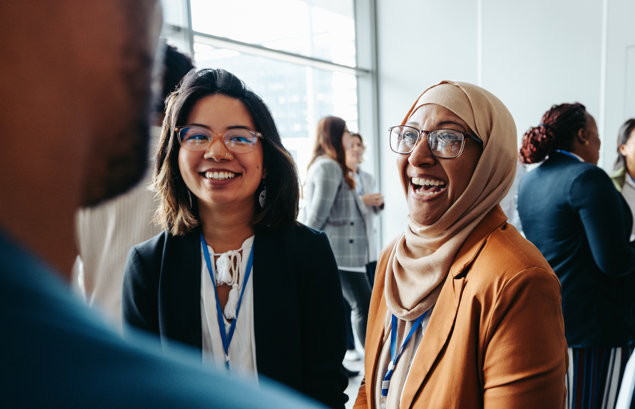 Female colleagues interacting at a corporate workshop, sharing happy smiles and engaging in lively conversations, promoting teamwork and networking in a professional setting.