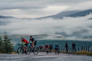 A group of cyclists rides along a foggy mountain road, enveloped in mist, showcasing the beauty of nature and adventure.