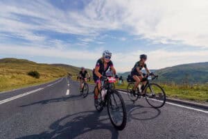 A trio of cyclists rides along a mountain road, showcasing the beauty of nature and the thrill of outdoor adventure.