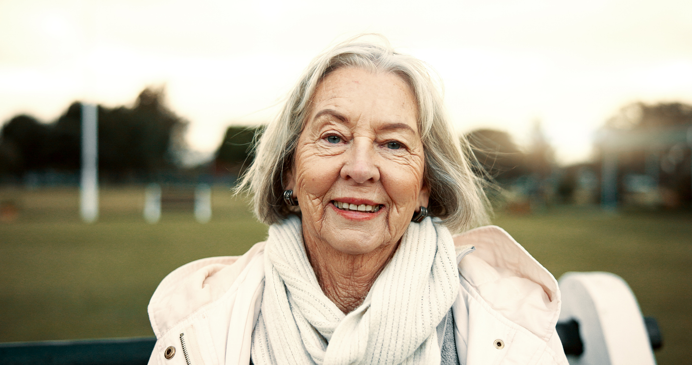 Face, senior woman and smile on park bench on vacation, holiday or travel in winter. Portrait, happy and elderly person in nature, garden or outdoor for wellness, freedom and relax in retirement